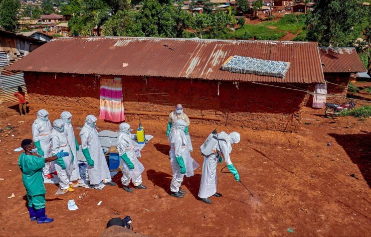 Red Cross workers wearing personal protective equipment walk in a formation as they disinfect the ground outside the house of an unidentified man who died of Ebola.