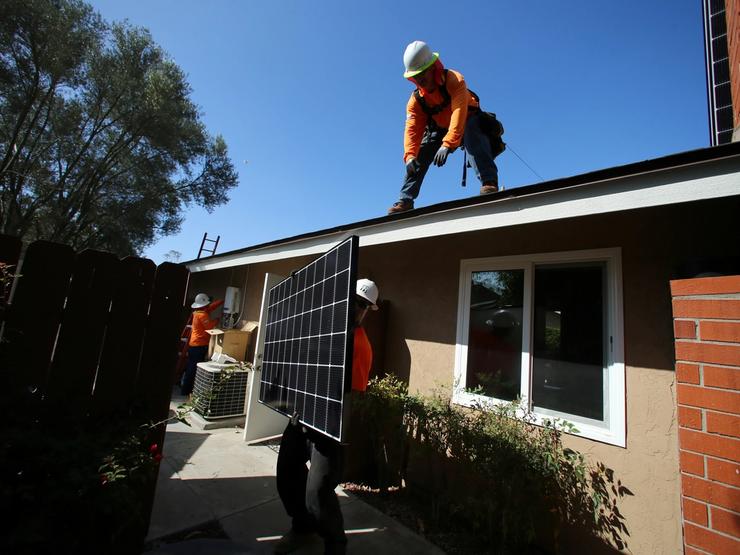 Workers lift a solar panel onto a roof during a residential solar installation in Scripps Ranch, San Diego.