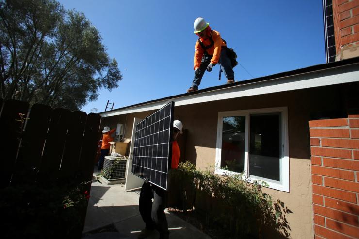 Workers lift a solar panel onto a roof during a residential solar installation in Scripps Ranch, San Diego.