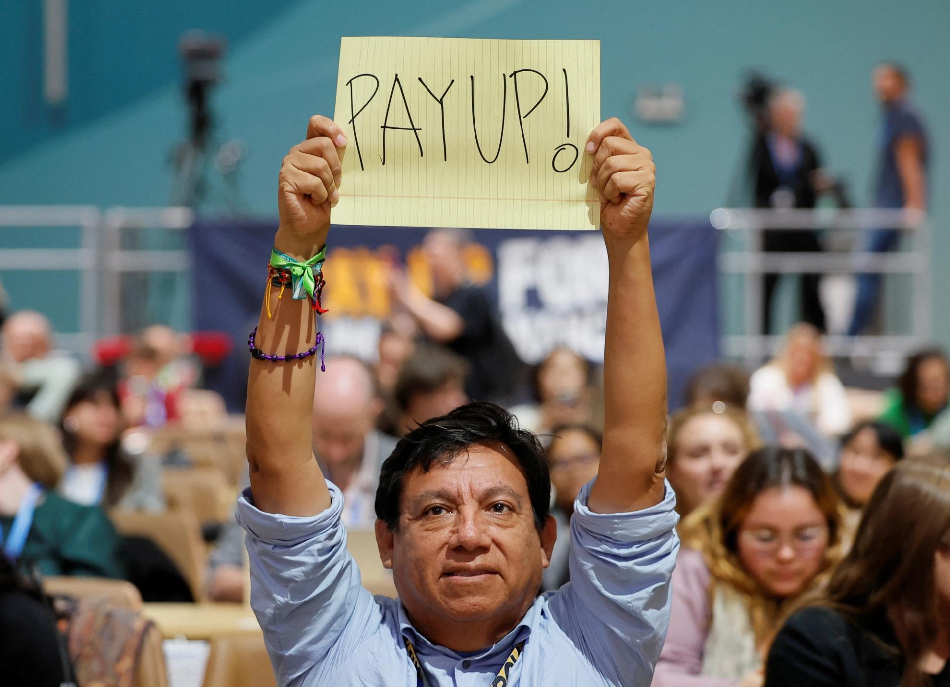 An activist holds up a sign at COP29 that says: “PAY UP!”