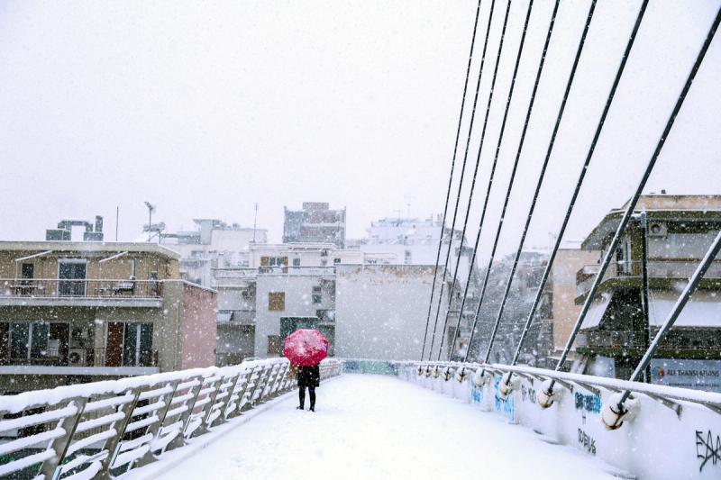 A woman holding an umbrella walks on a pedestrian bridge, during snowfall in Athens, Greece, February 6, 2023.