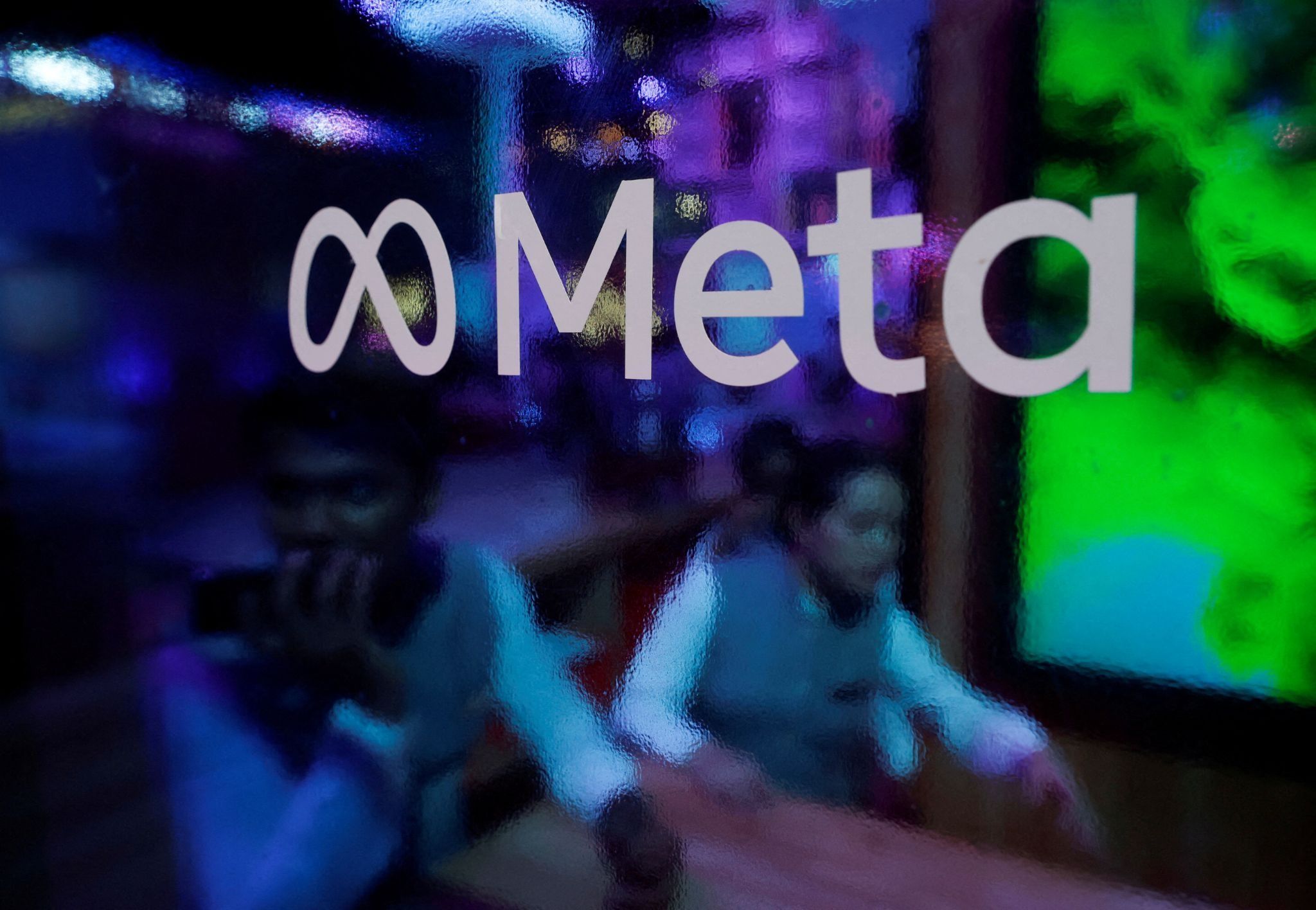 People are seen behind a logo of Meta Platforms. 