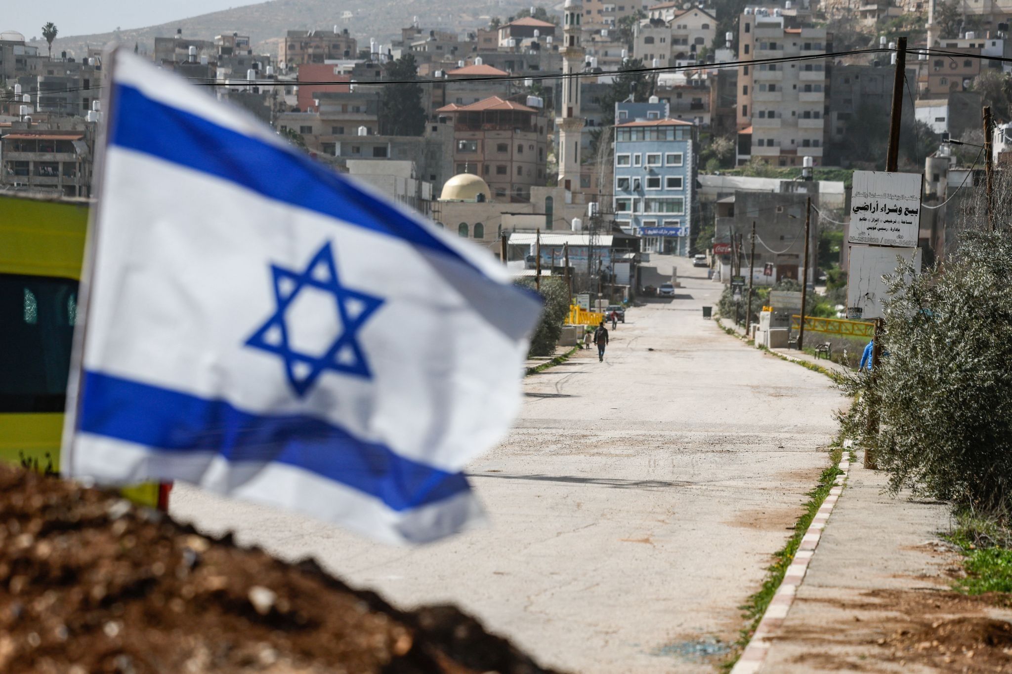 Israeli flag flutters at a dirt barrier that was recently placed by the Israeli military at the main entrance to Luban e-Sharkiya, in the Israeli-occupied West Bank