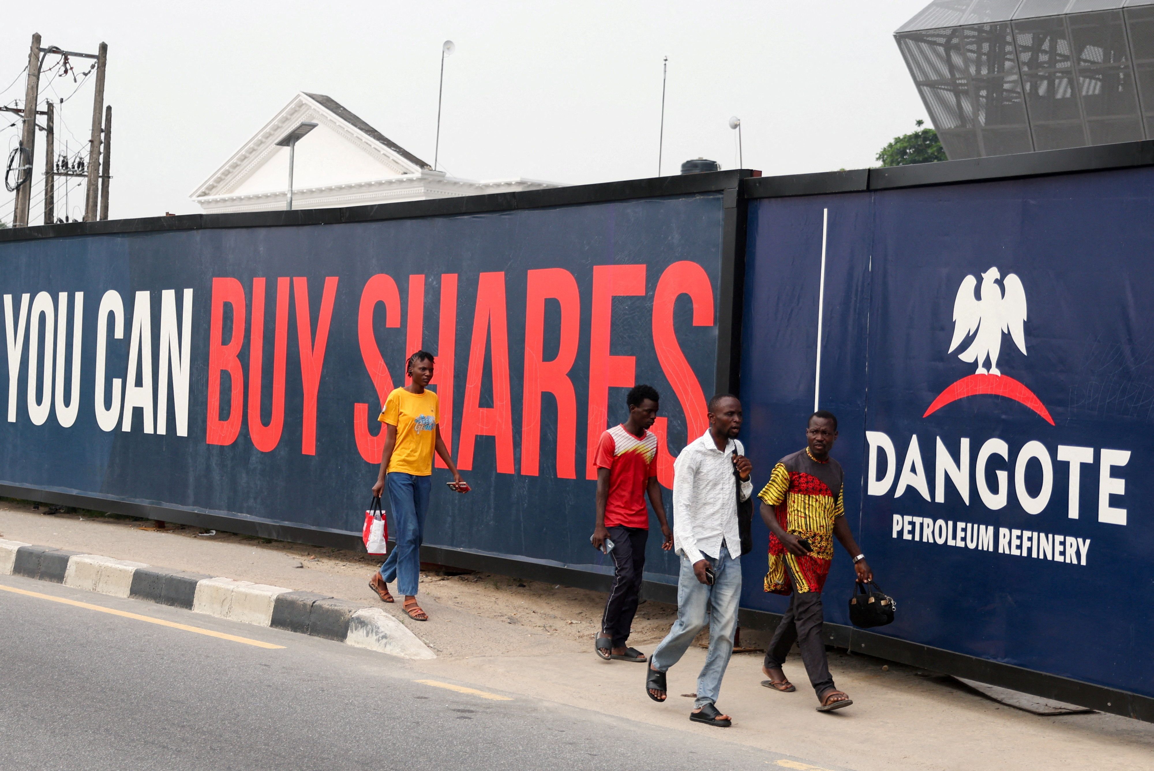 People walk past a billboard advertising Dangote Petroleum Refinery’s initial public offering.
