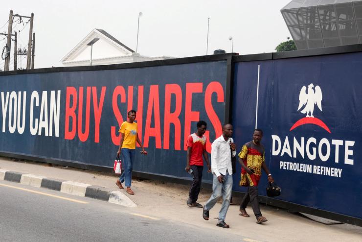 People walk past a billboard advertising Dangote Petroleum Refinery’s initial public offering.