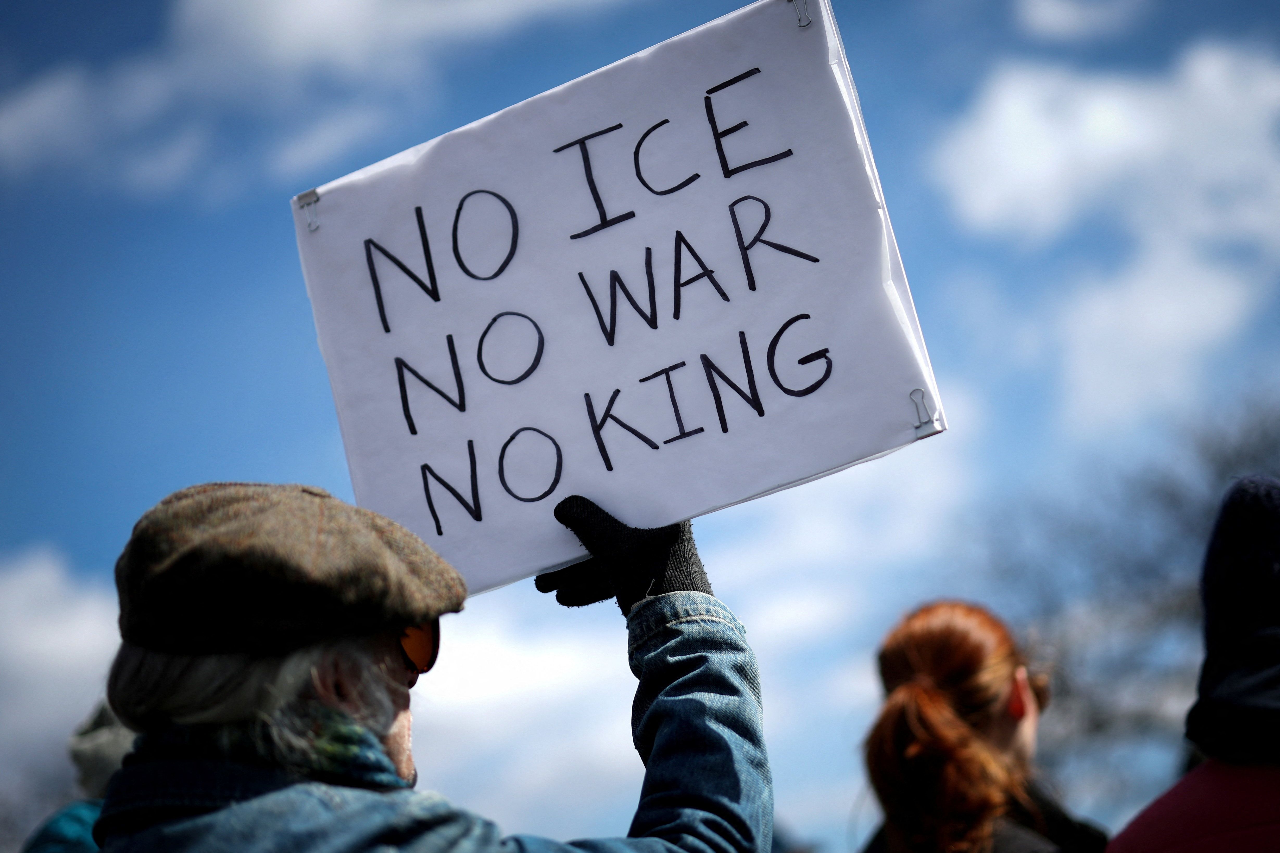 Protestor holds sign reading “NO ICE NO WAR NO KING”