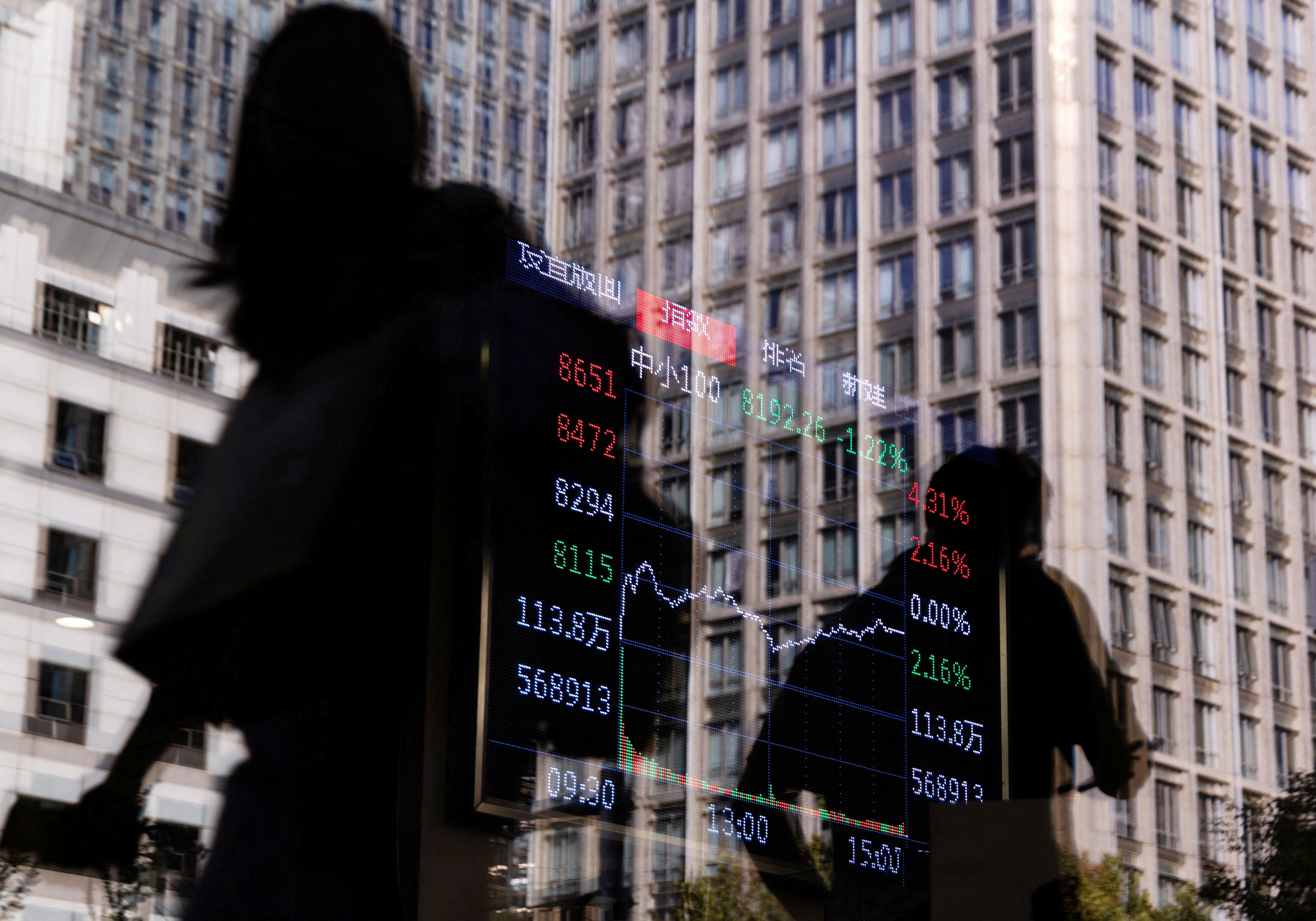 People walk past a brokerage house, as an electronic board displays stock index information graph in Beijing.
