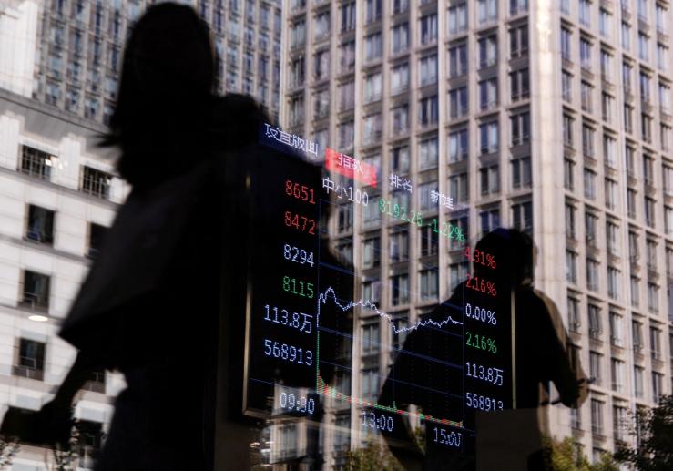 People walk past a brokerage house, as an electronic board displays stock index information graph in Beijing.