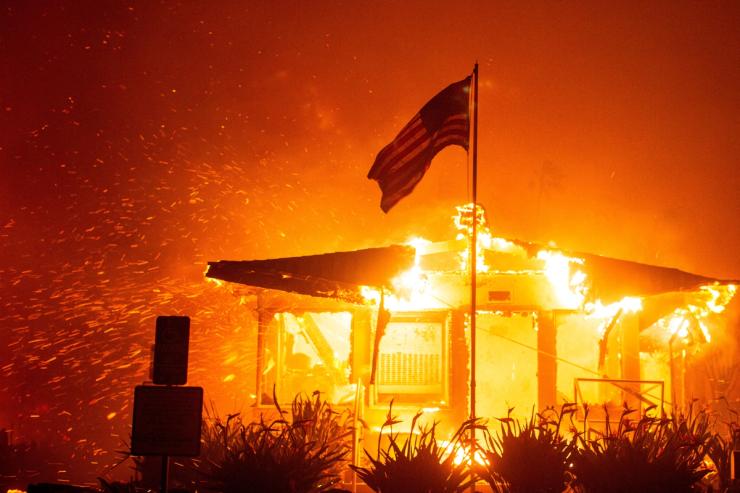 A U.S flag flies as fire engulfs a structure while the Palisades Fire burns during a windstorm on the west side of Los Angeles, California, U.S. January 7, 2025.