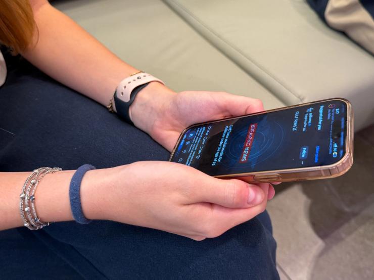 A teenage girl holds her mobile phone displaying a news alert on social media.