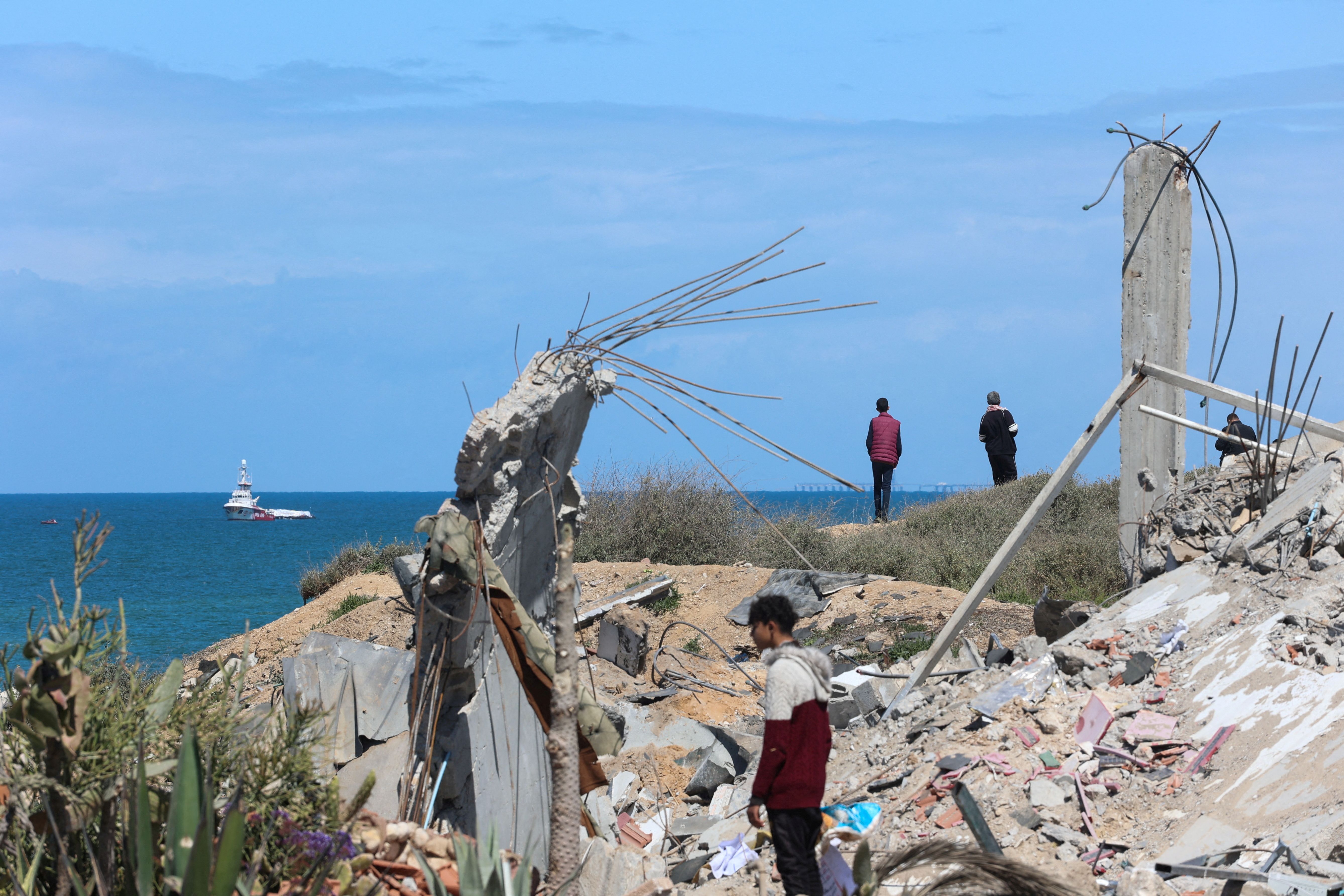 People watch as ship carrying aid sails off the shore of Gaza, amid the ongoing conflict between Israel and the Palestinian Islamist group Hamas, as seen from central Gaza Strip, March 15, 2024. REUTERS/Ahmed Zakot TPX IMAGES OF THE DAY