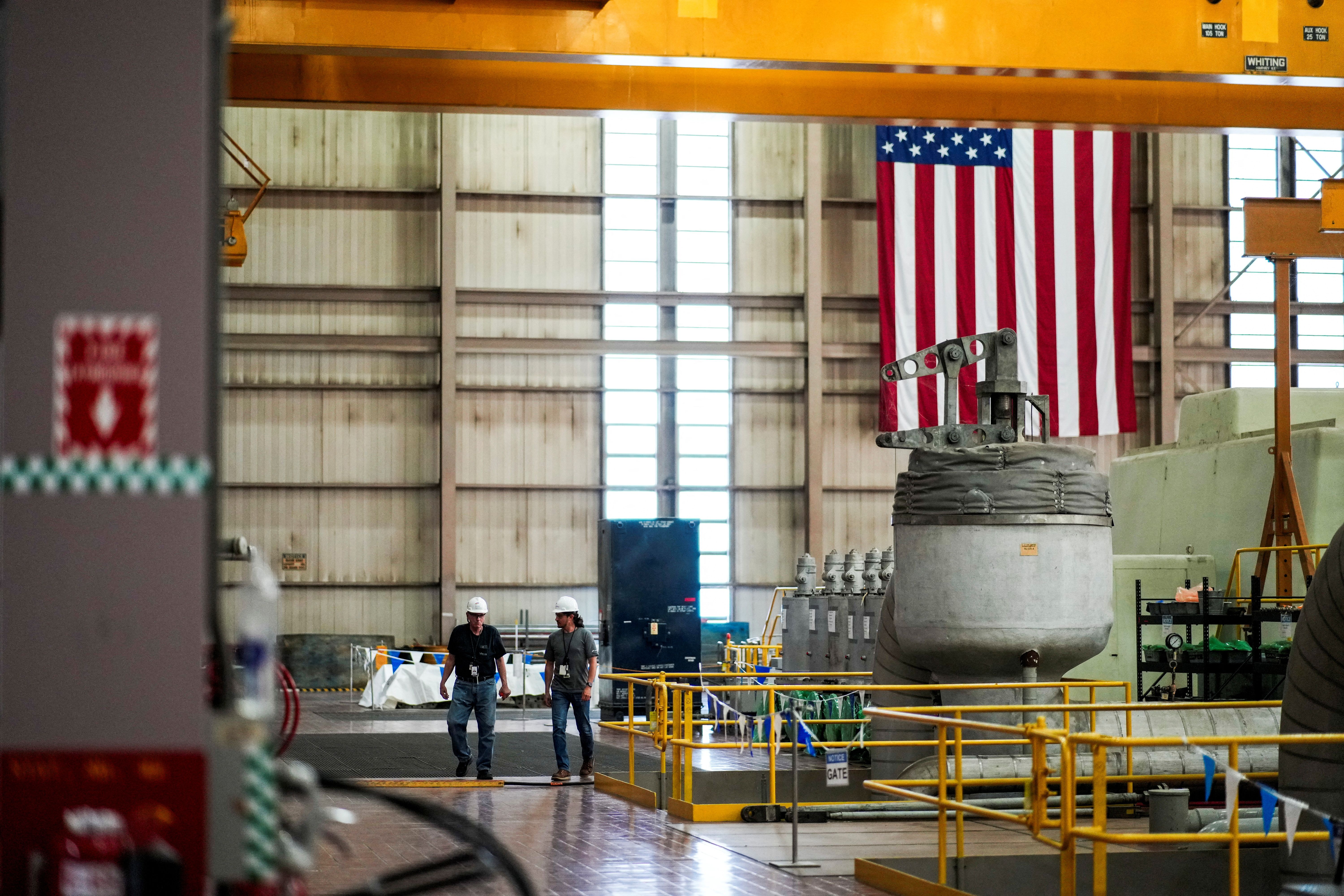 Constellation Energy workers walk near a generator in the turbine hall at the former Three Mile Island Nuclear power plant.
