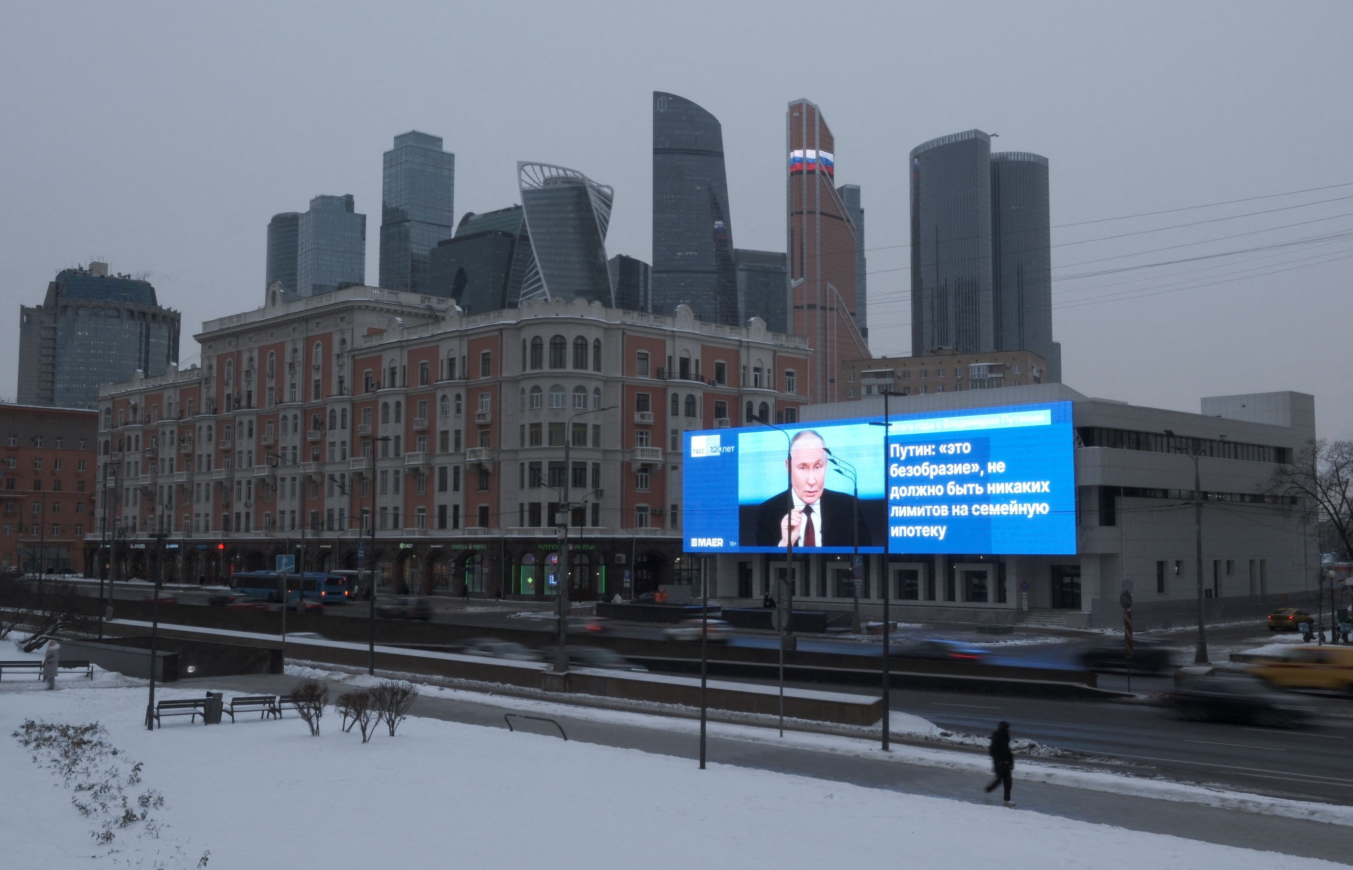 Cars drive past an electronic screen, which shows an image of Russian President Vladimir Putin and a quote from his annual televised year-end press conference and phone-in.