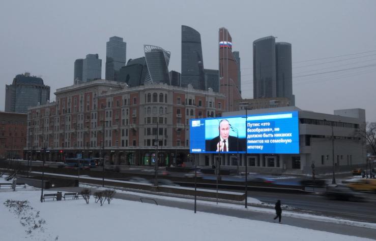 Cars drive past an electronic screen, which shows an image of Russian President Vladimir Putin and a quote from his annual televised year-end press conference and phone-in.