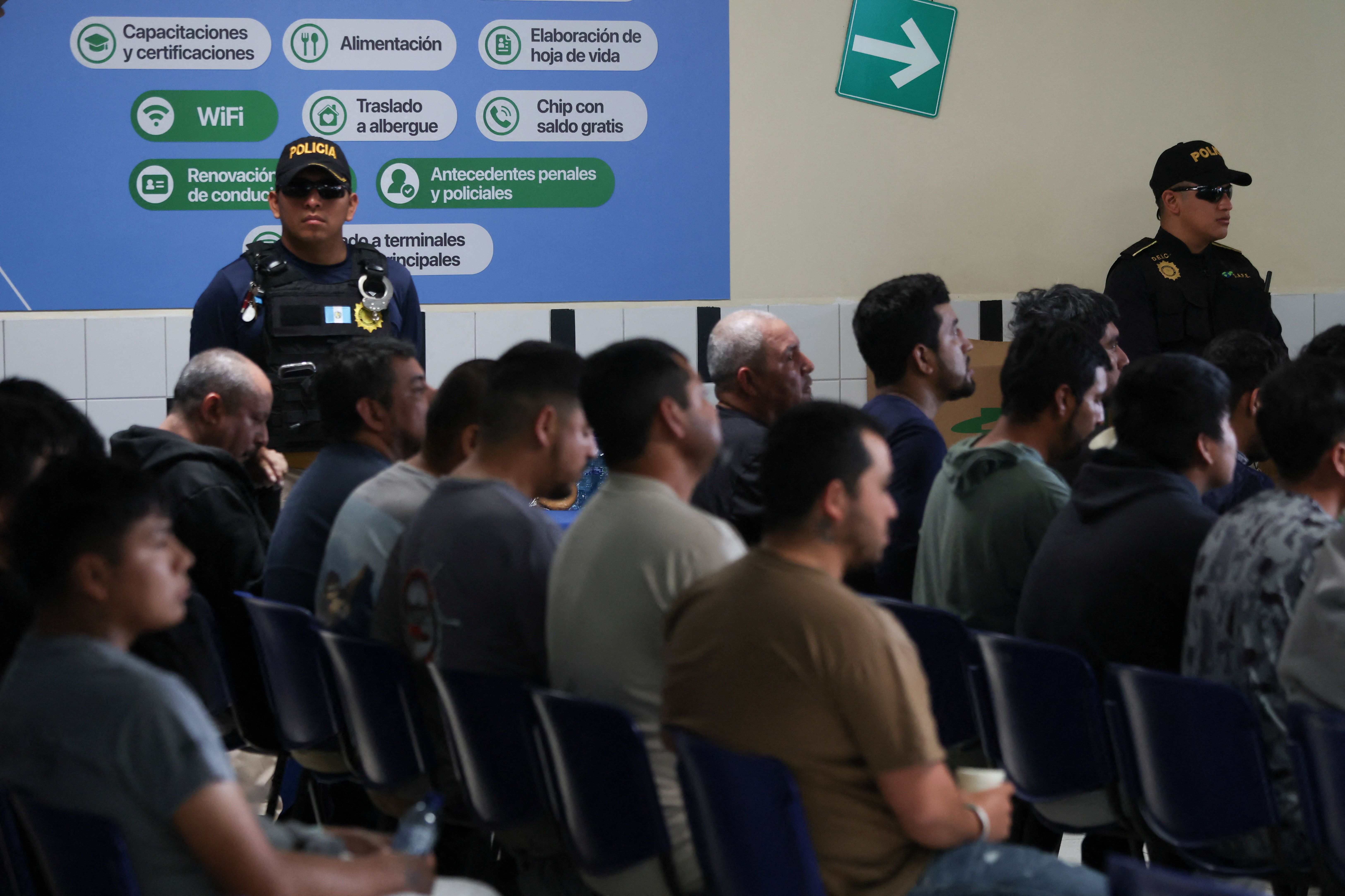 Police officers stand guard as Mexican migrants deported from the United States wait.