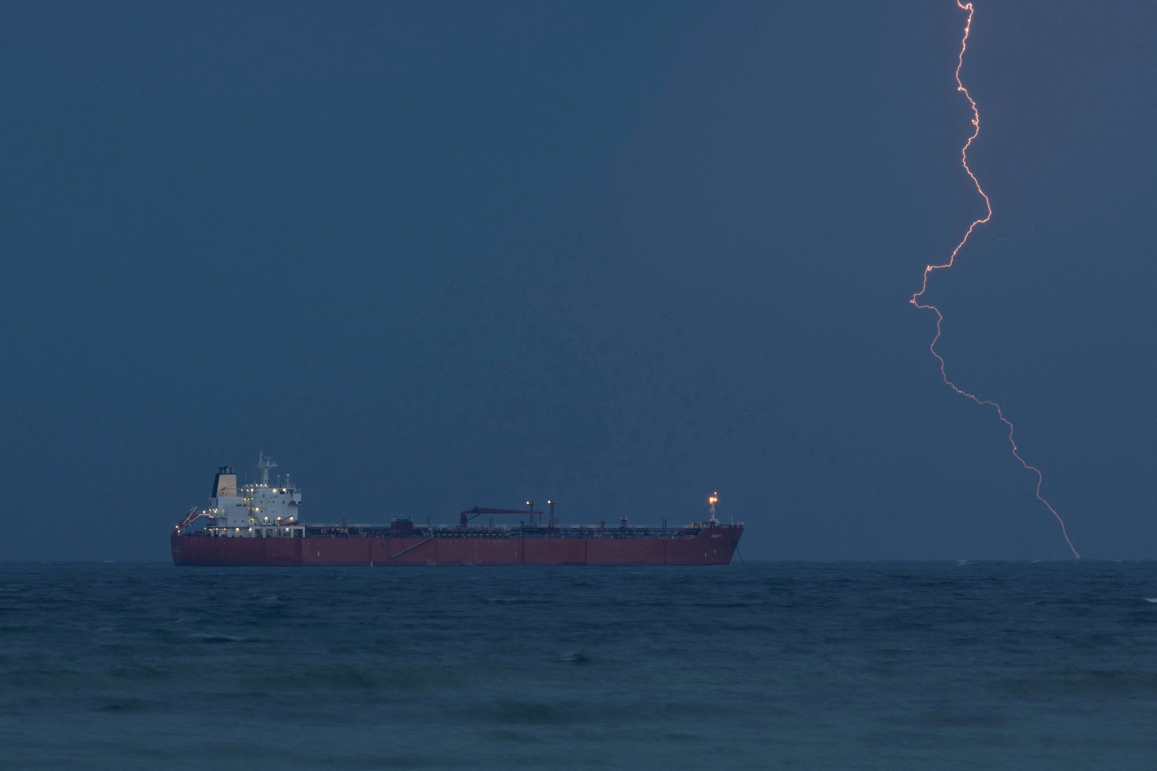 The tanker RARITY sits at anchor as lightning flashes in the distance.