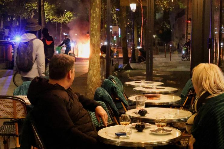 Customers at a cafe watch a fire set by rioters at the end of a day of nationwide cost-of-living protests in Paris, France, Oct. 17, 2026