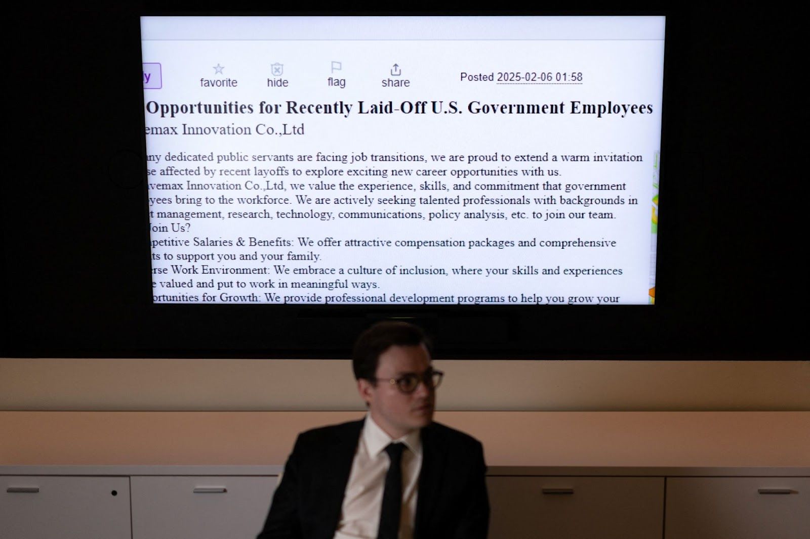 A senior analyst on emerging threats at the Foundation for Defense of Democracies sits in front of a screen projection of a post soliciting recently laid off US government employees.