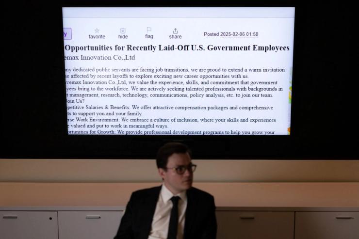 A senior analyst on emerging threats at the Foundation for Defense of Democracies sits in front of a screen projection of a post soliciting recently laid off US government employees.