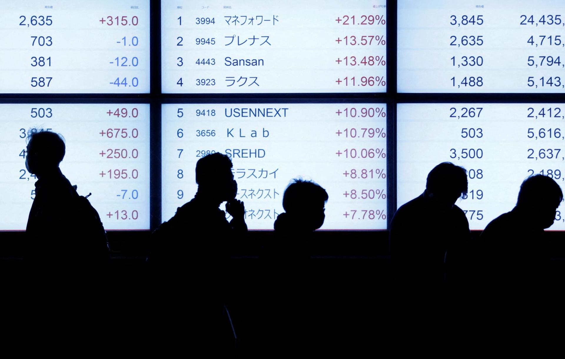 Passersby are silhouetted as they walk past in front of an electric stock quotation board outside a brokerage in Tokyo, Japan