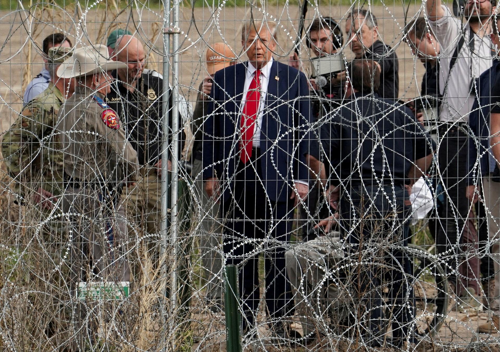 Donald Trump standing behind a barbed wire fence.