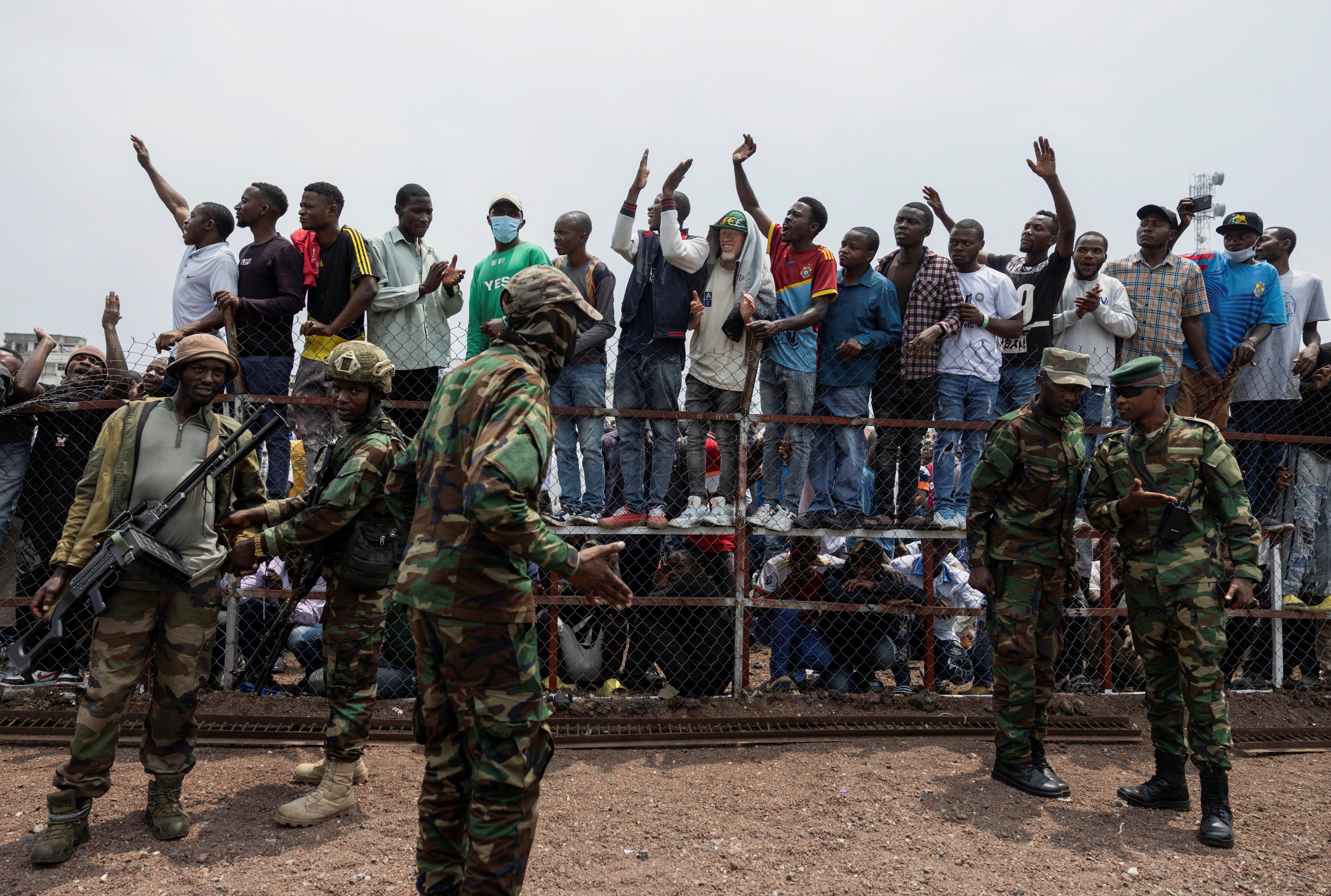 M23 rebels stand guard near civilians during a meeting at the Stade de l’Unite in Goma