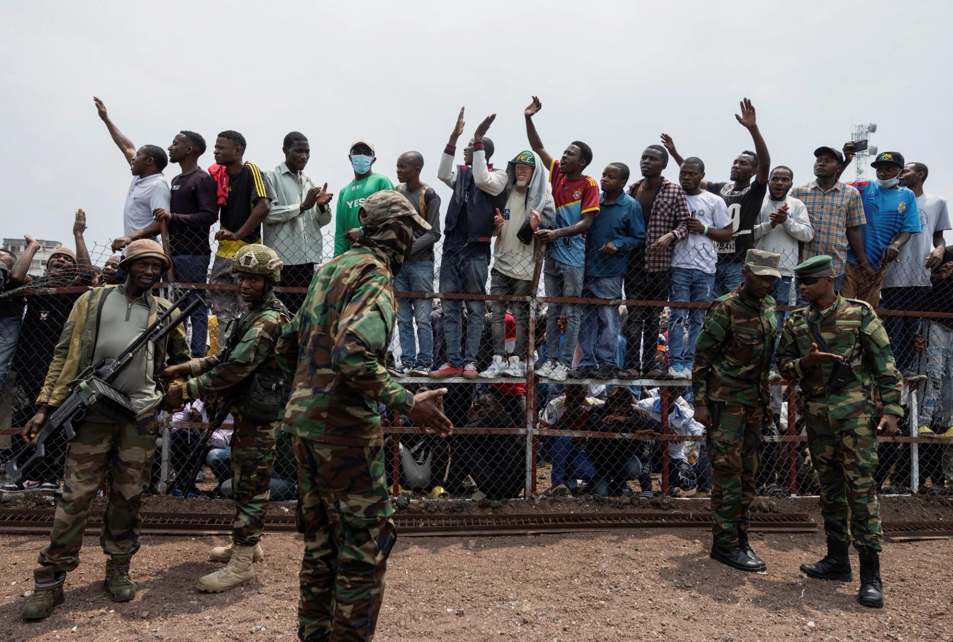 M23 rebels stand guard near civilians during a meeting at the Stade de l’Unite in Goma