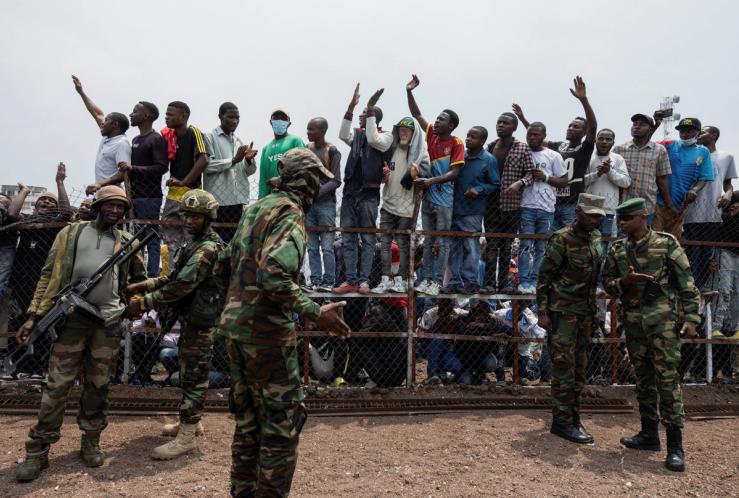 M23 rebels stand guard near civilians during a meeting at the Stade de l’Unite in Goma