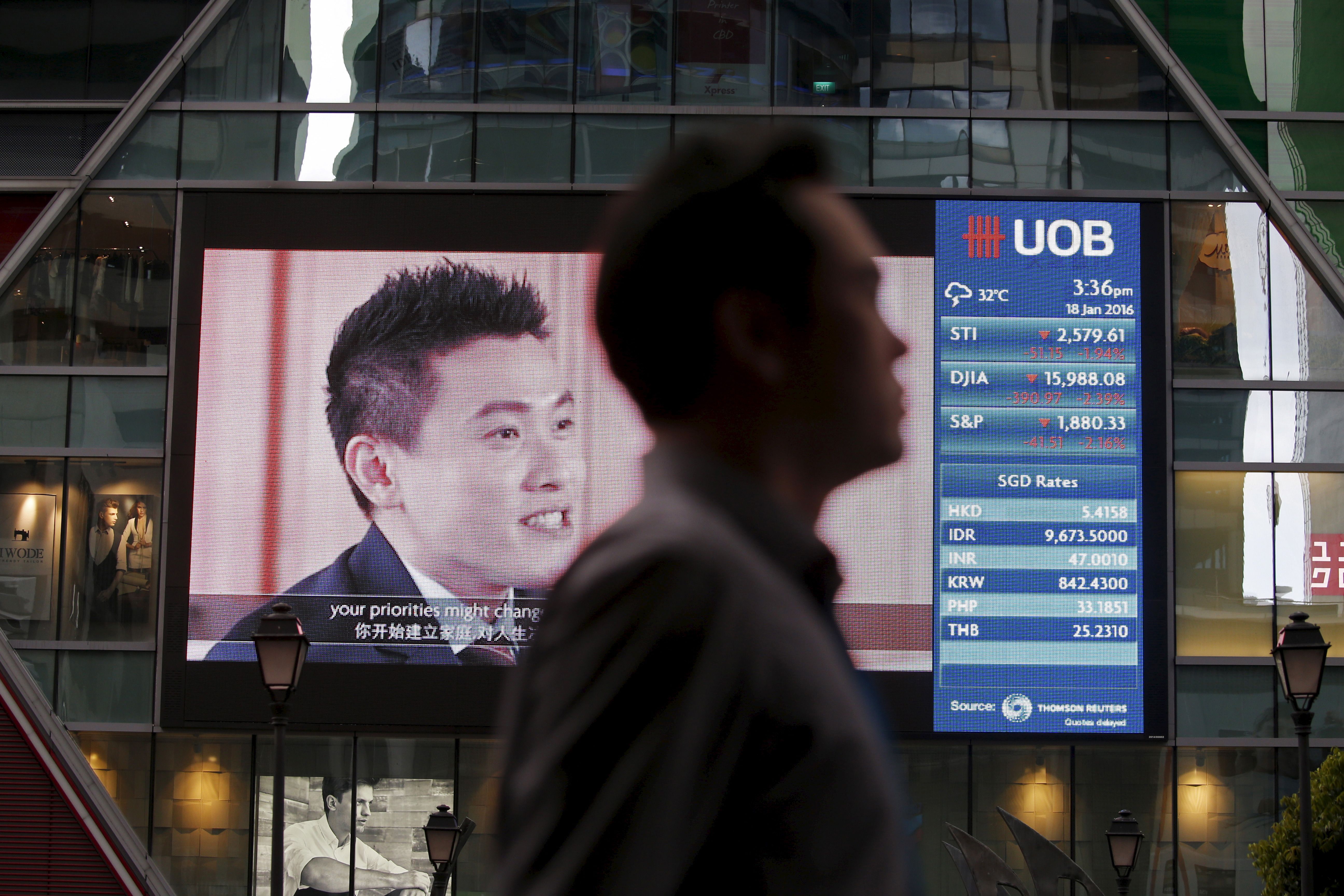 A man passes a board showing the decline of Straits Times Index (STI), Dow Jones Industrial Average (DJIA) and the Standard and Poor’s (S&P) index at the central business district in Singapore