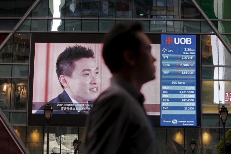 A man passes a board showing the decline of Straits Times Index (STI), Dow Jones Industrial Average (DJIA) and the Standard and Poor’s (S&P) index at the central business district in Singapore