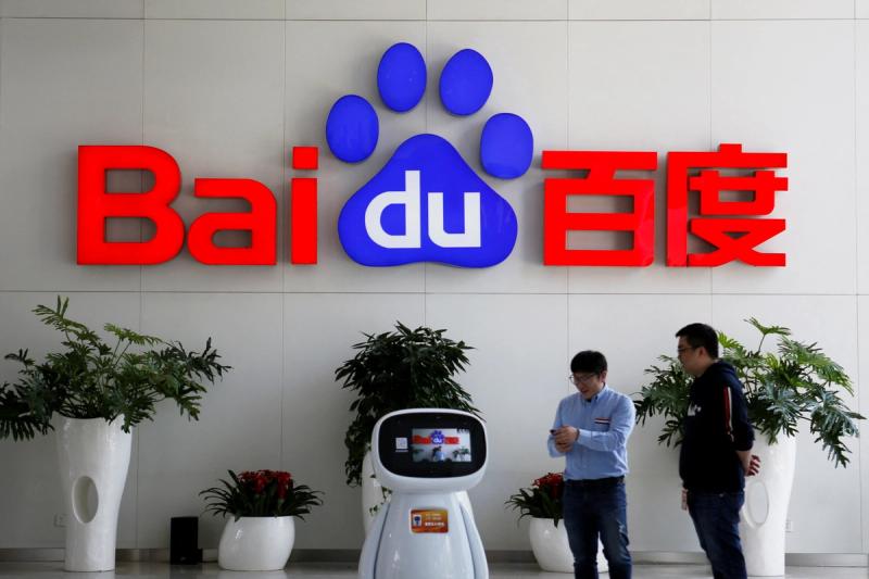 Men interact with a Baidu AI robot near the company logo at its headquarters in Beijing, China April 23, 2021.