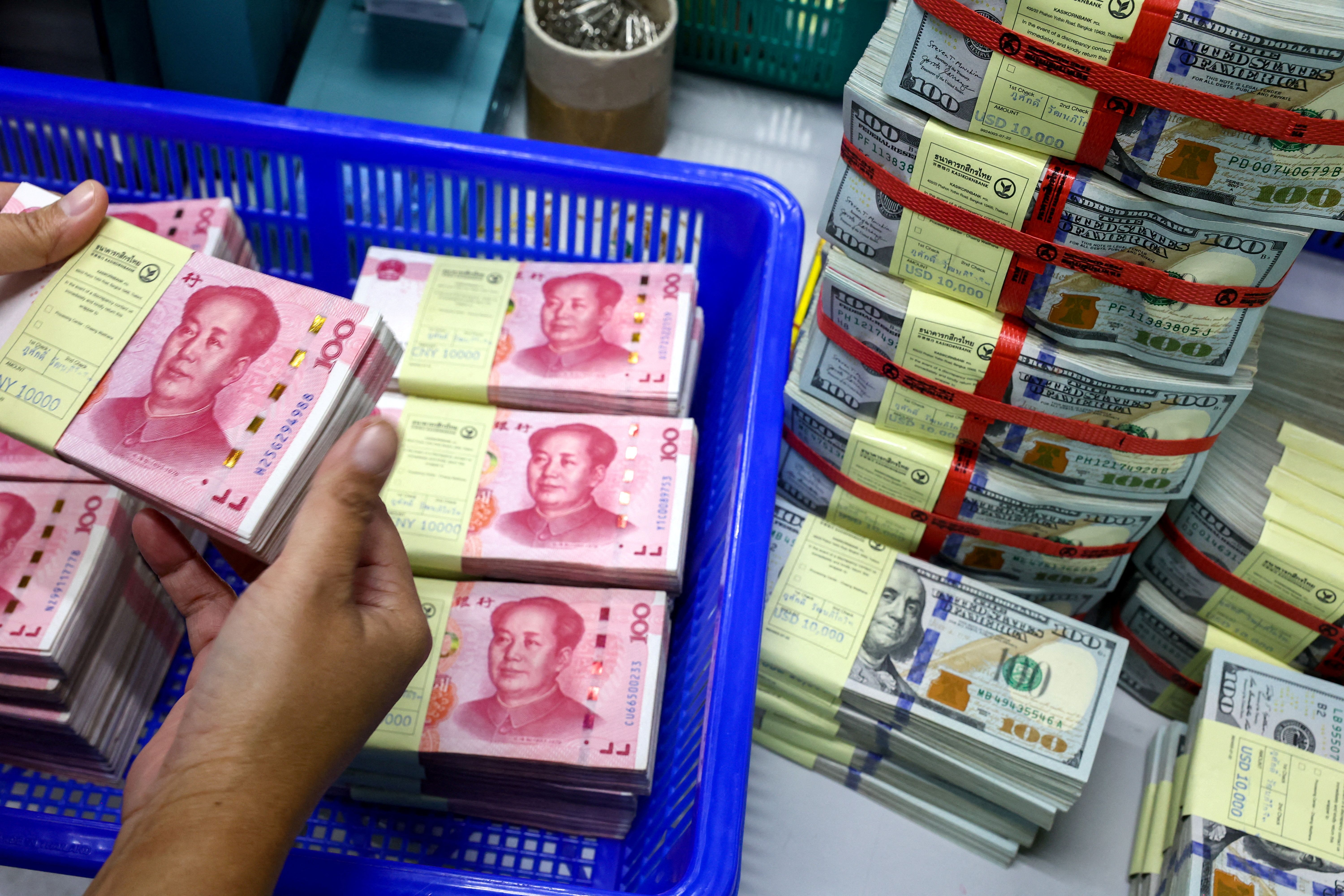 FILE PHOTO: A bank employee counts China’s renminbi (RMB) or yuan notes next to U.S. dollar notes at a Kasikornbank in Bangkok, Thailand, January 26, 2023. REUTERS/Athit Perawongmetha/File Photo