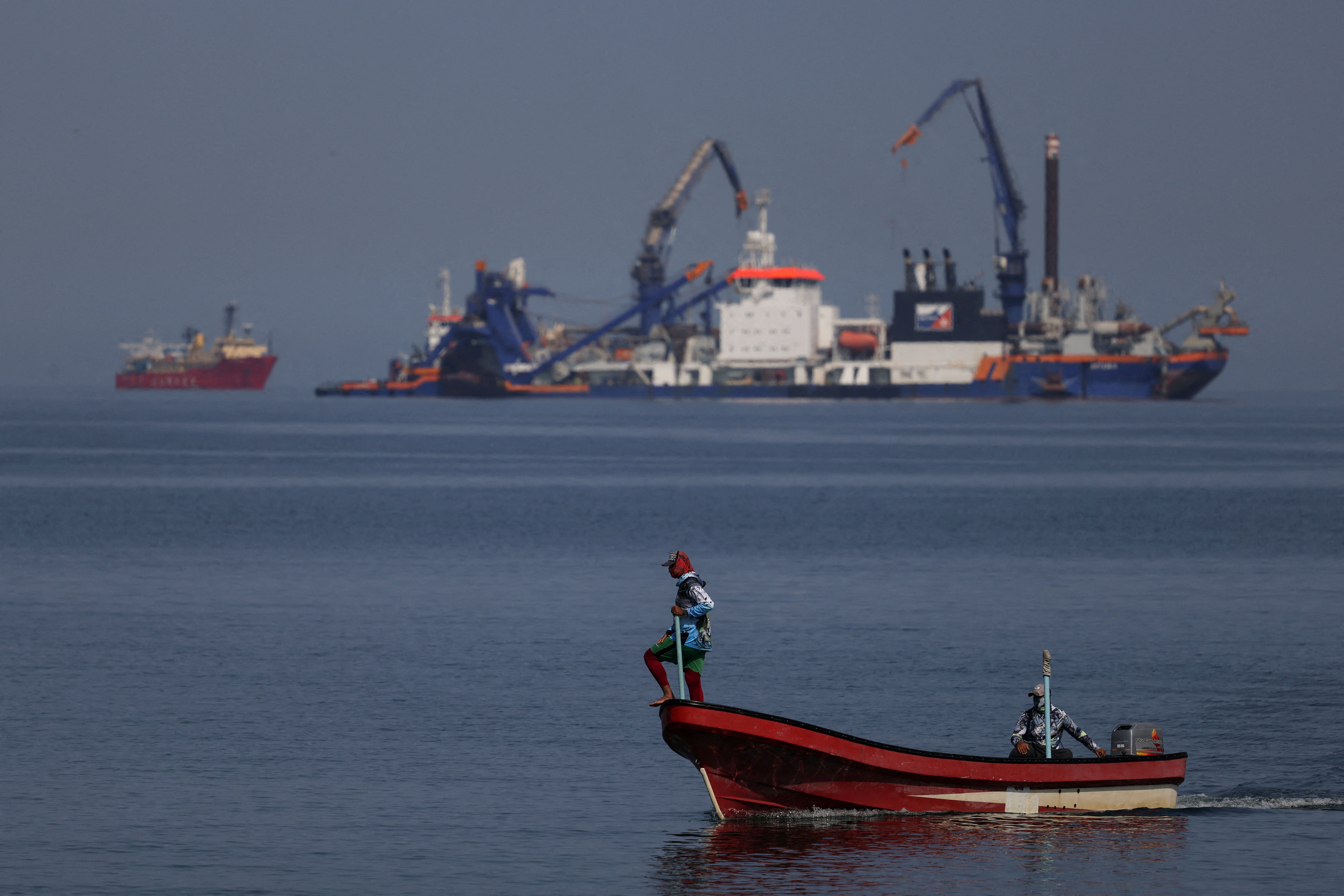 A fisherman stands on a boat near vessels off the coast of Oman 