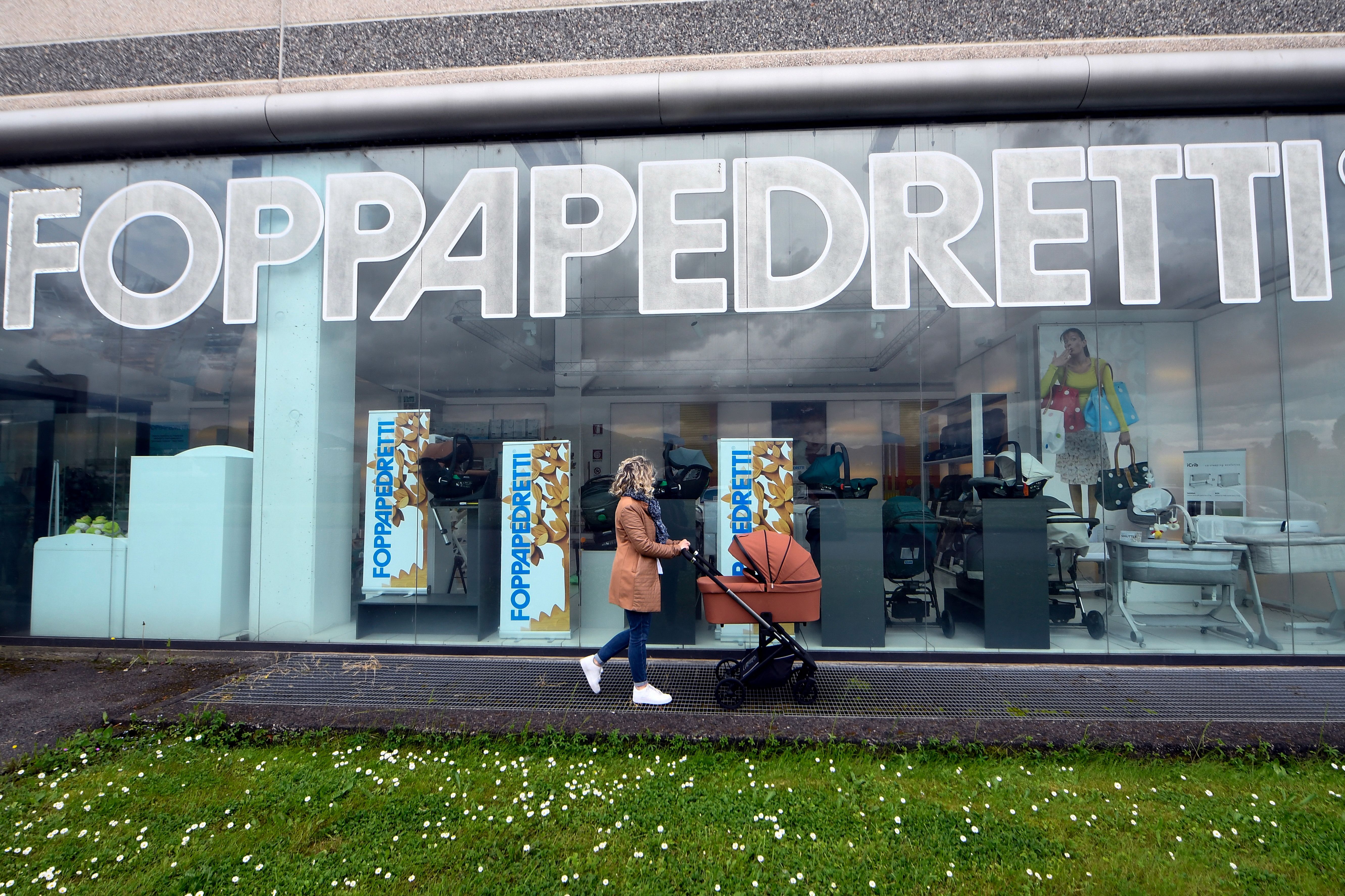 A woman pushing a baby stroller walks past the showroom of manufacturer Foppapedretti’s factory in Bolgare, near Bergamo, Italy.