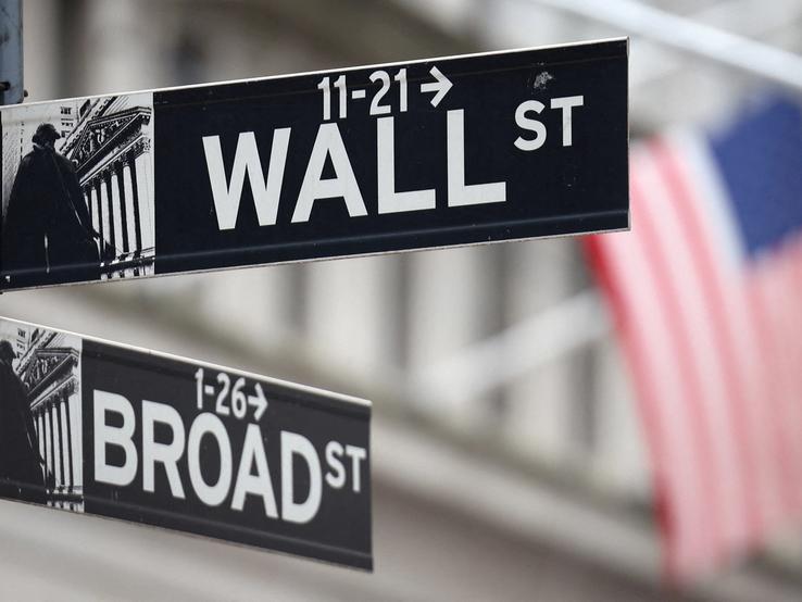A Wall Street sign hangs in front of a US flag outside the New York Stock Exchange (NYSE)