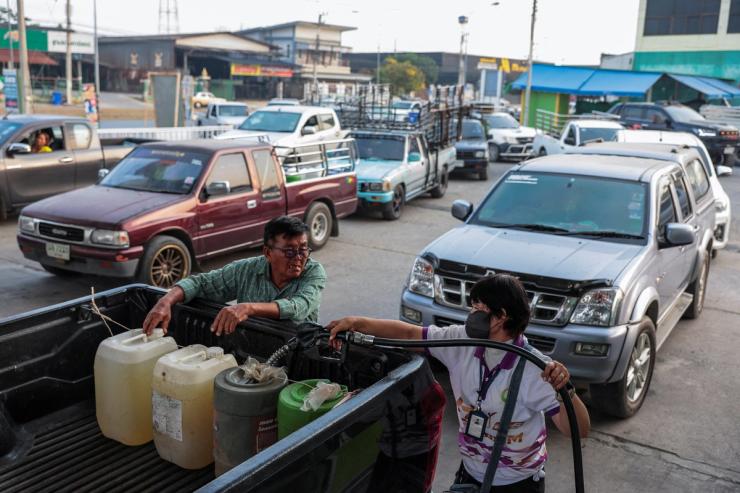 A worker fills plastic jerrycans with fuel as drivers queue in traffic at a fuel station in Thailand.
