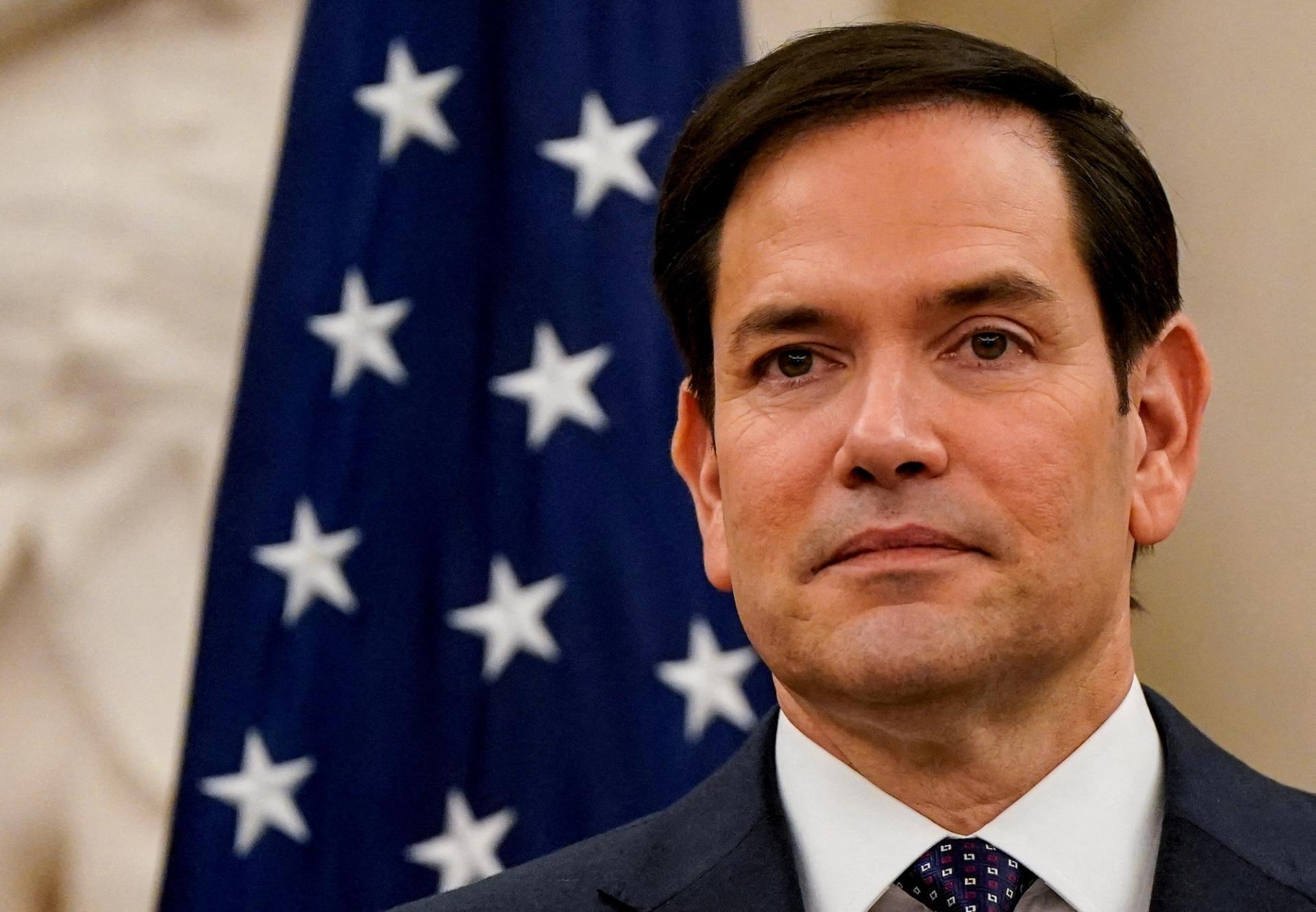 Marco Rubio standing in front of a US flag