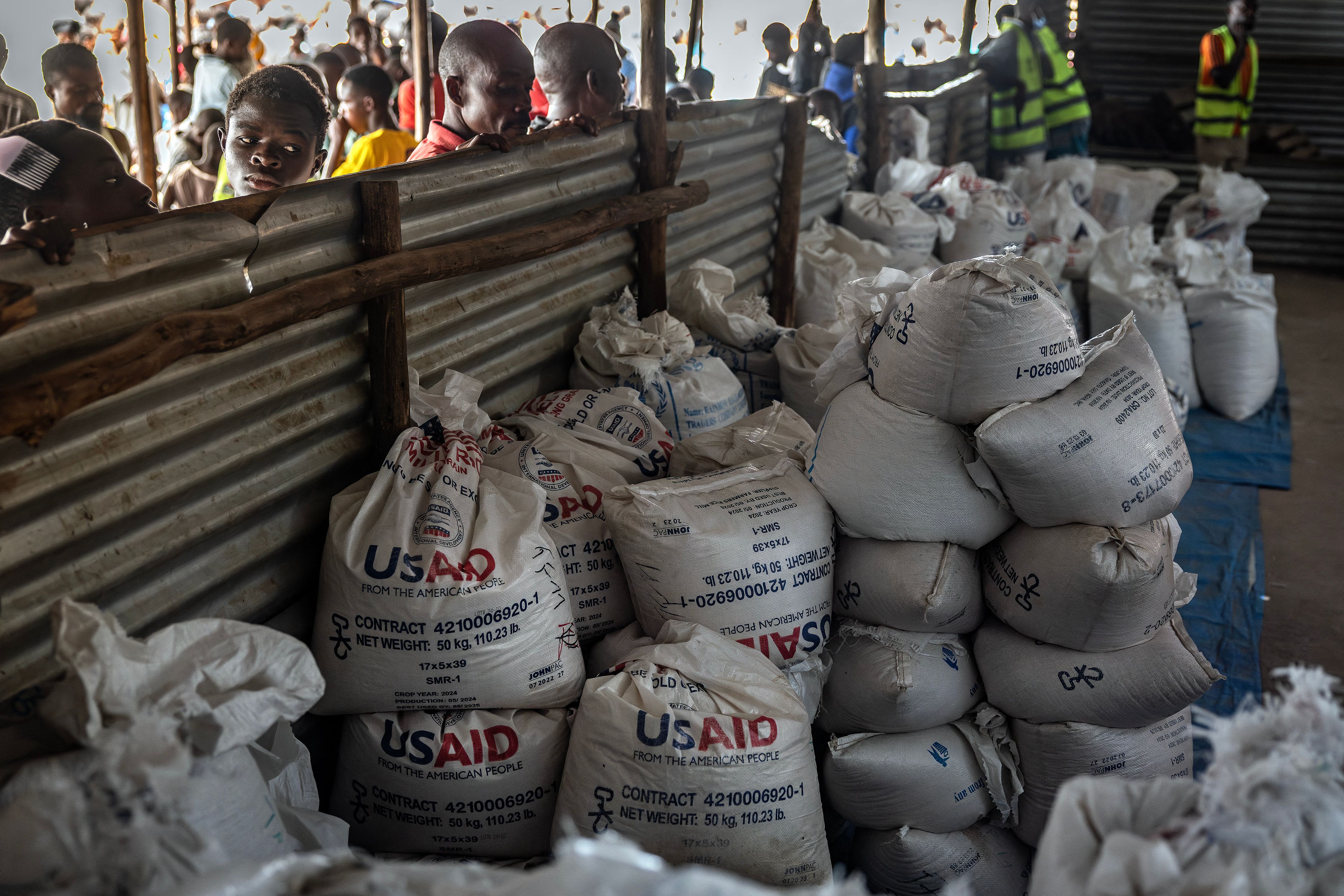 Congolese refugees look through a corrugated metal fence at the final batches of food delivered by the now-dismantled United States Agency for International Development.