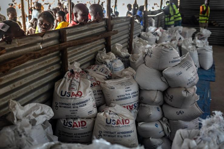 Congolese refugees look through a corrugated metal fence at the final batches of food delivered by the now-dismantled United States Agency for International Development.