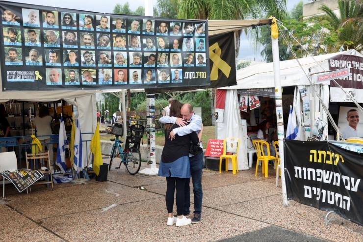 People hug next to banner with photos of hostages at the “Hostages square.”