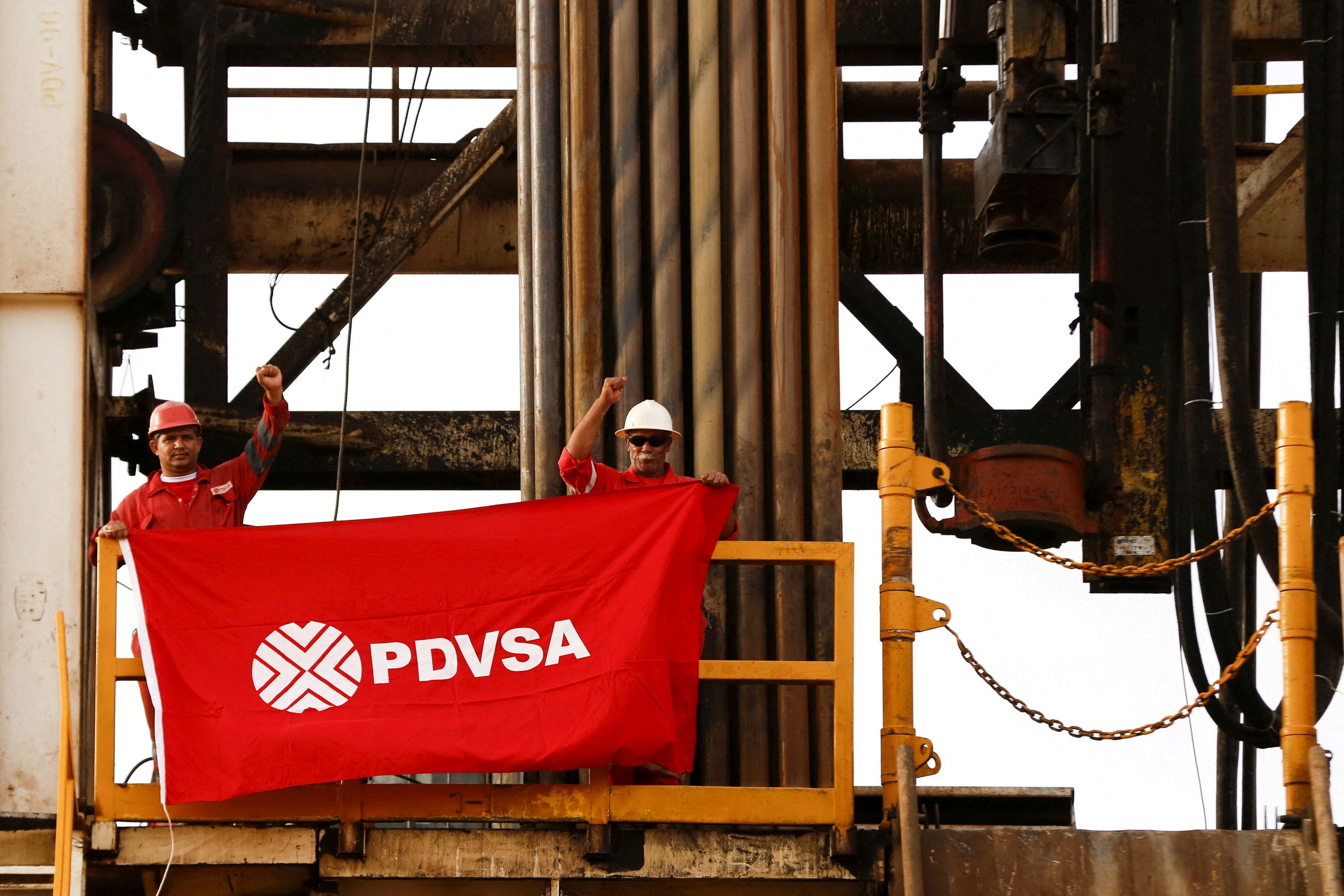 Oilfield workers hold a flag with the corporate logo of Venezuela’s state oil company PDVSA.