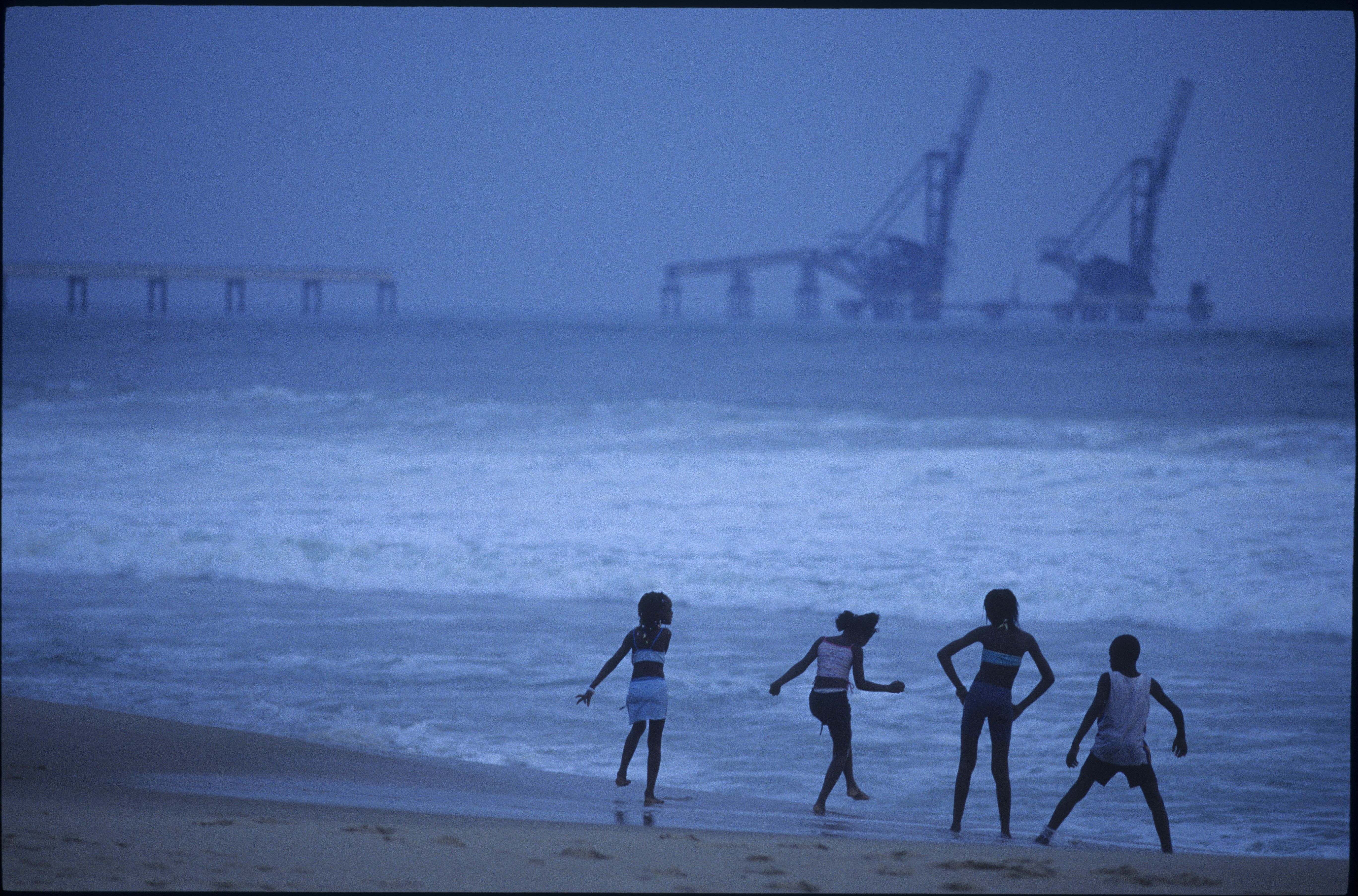 Children playing on the beach, facing oil equipment in Pointe Noire, Congo.