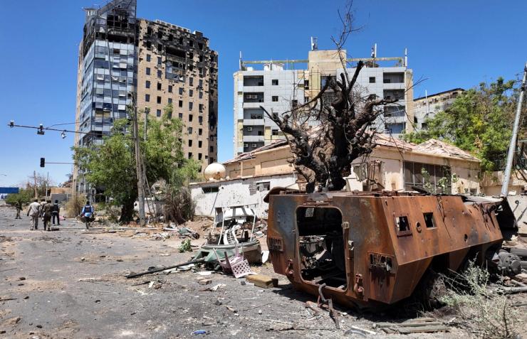 Members of army walks near a destroyed military vehicle and bombed buildings in Sudan.