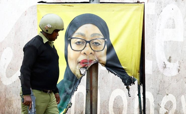 A Tanzanian riot police officer walks past a poster of President Samia Suluhu Hassan at the Namanga Border with Kenya Oct. 30.