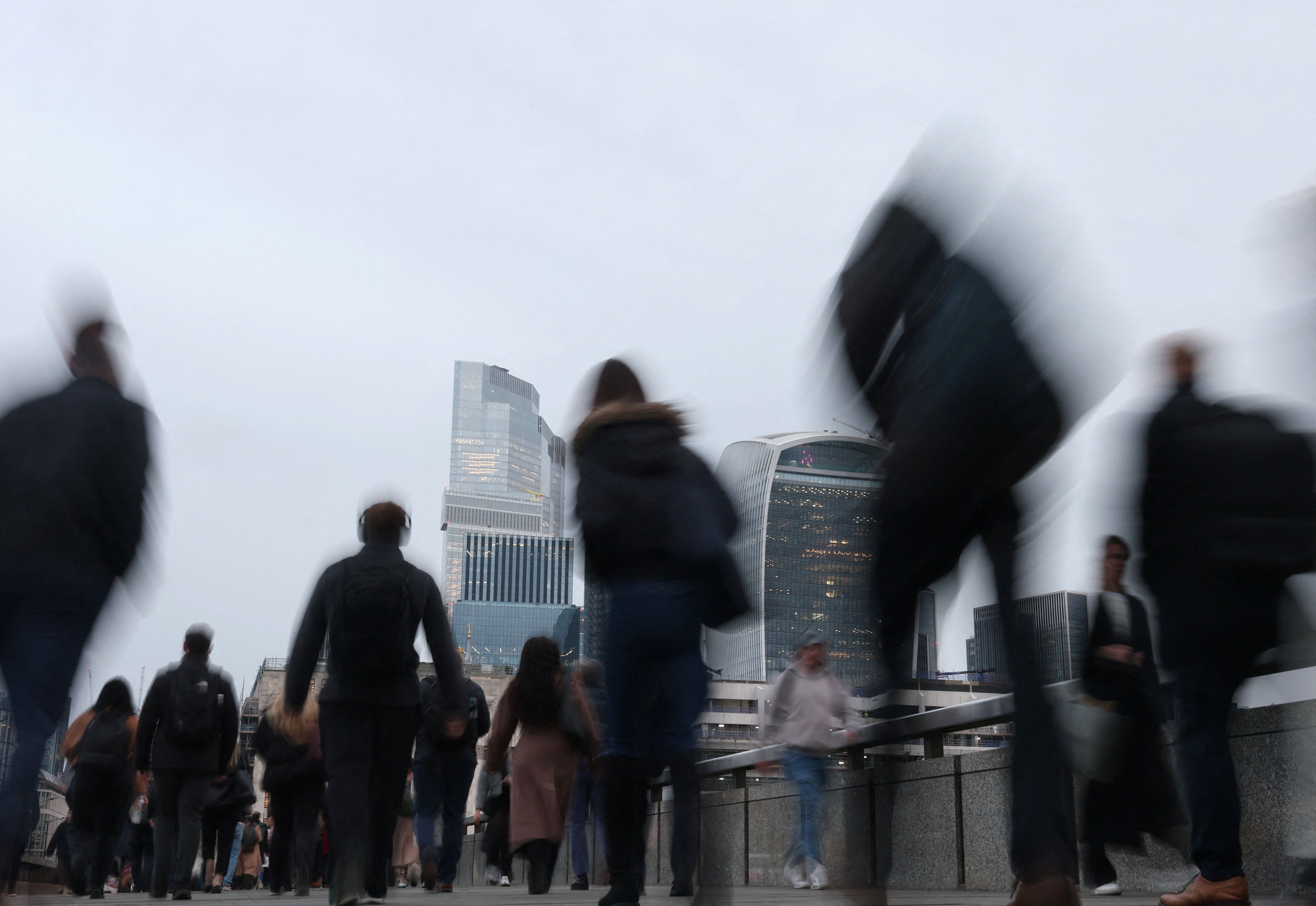 Workers cross London Bridge during the morning rush-hour with skyscrapers of the City of London financial district seen behind, in London, Britain, 