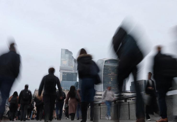 Workers cross London Bridge during the morning rush-hour with skyscrapers of the City of London financial district seen behind, in London, Britain,
