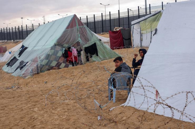 Displaced Palestinians, who fled their houses due to Israeli strikes, amid the ongoing conflict between Israel and the Palestinian Islamist group Hamas, sit outside a tent at the border with Egypt, amid fears of an Israeli ground assault in Rafah, in the southern Gaza Strip February 18, 2024. REUTERS/Saleh Salem