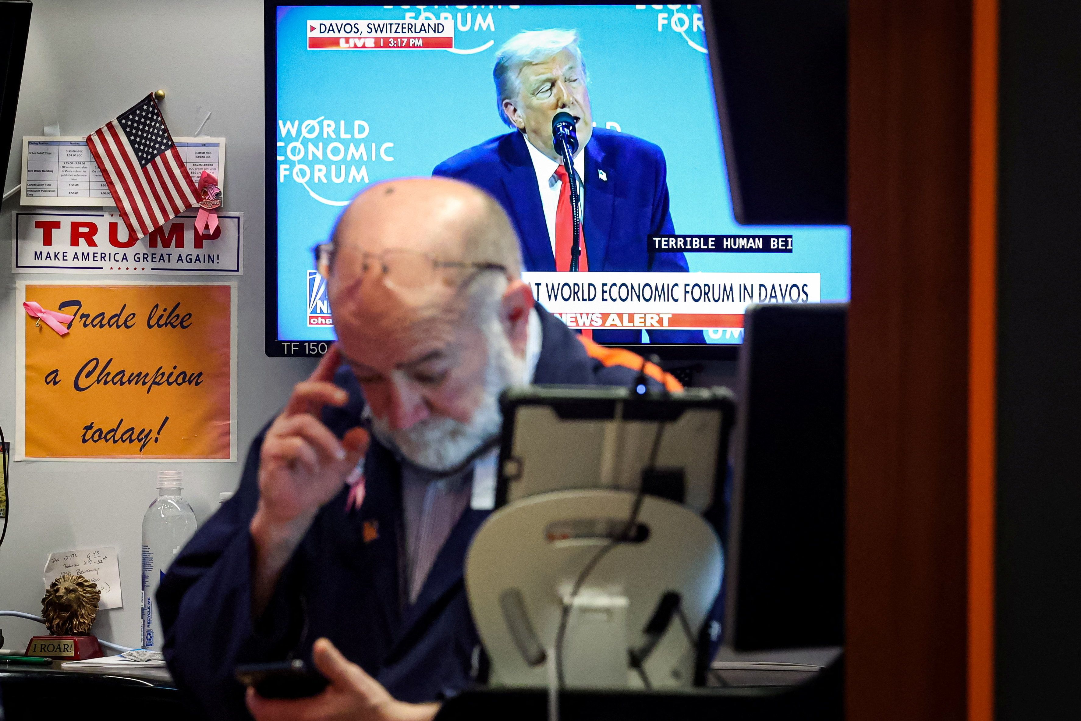 A trader works, as a screen displays U.S. President Donald Trump speaking at the World Economic Forum (WEF)