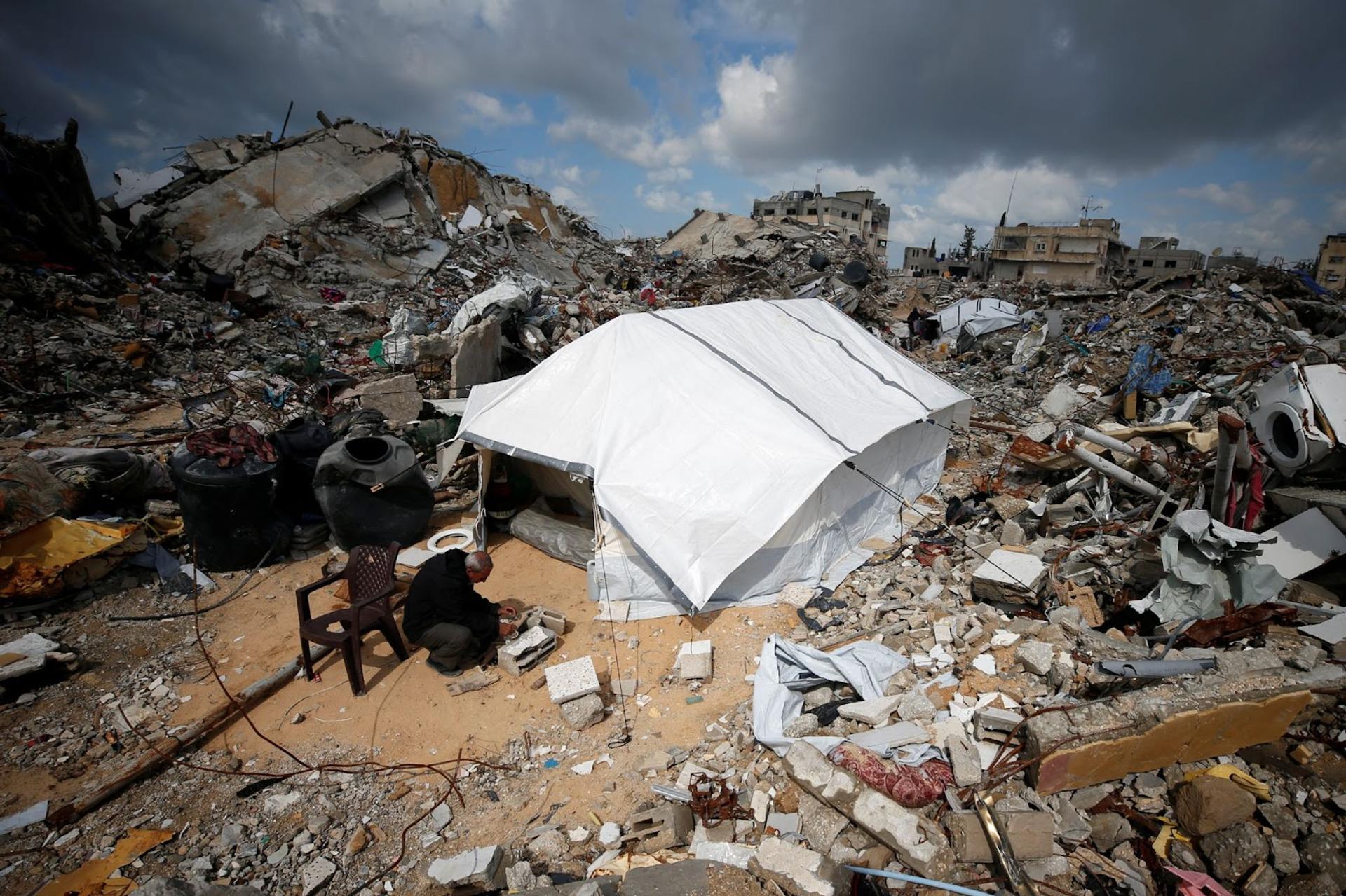 A Palestinian man works to light a fire outside his tent, set up near the rubble of his house in Gaza