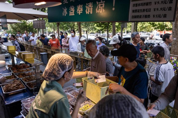 People queue at a setup of stalls selling food to passersby next to Beiyuan Grand Hotel in Beijing, China.